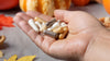 Hand holding a variety of supplement capsules. Background has orange and yellow leaves and multiple pumpkins. 