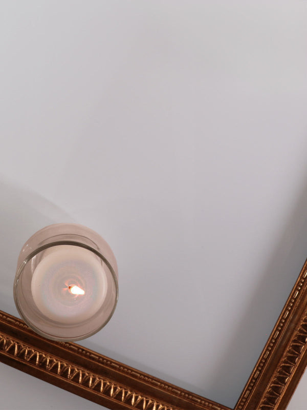 Candle in a glass holder on a white surface with a decorative mirror corner.