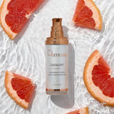 Osmosis Catalyst serum bottle surrounded by grapefruit slices on a textured white background