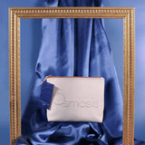White pouch with 'Osmosis' branding on a blue satin background, framed by a gold decorative border.